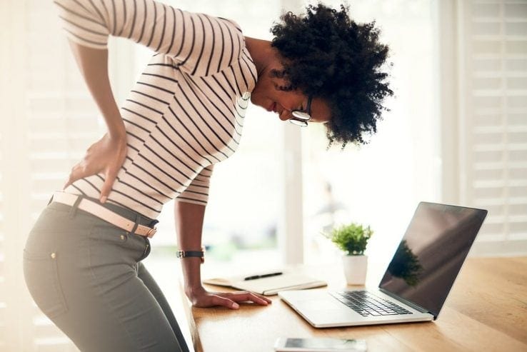 A woman leaning over her desk as she struggles with back pain