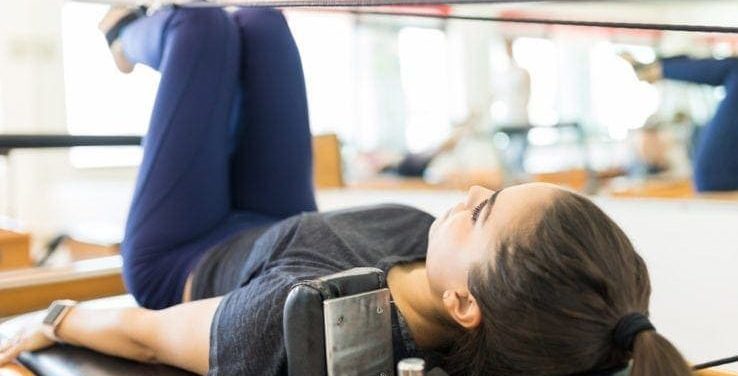 A woman using a pilates reformer machine in the gym