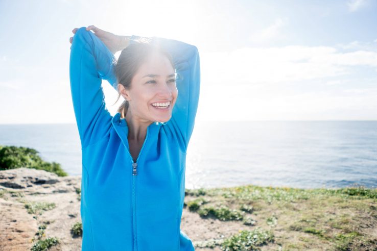 A woman smiling while stretching out her arms and back