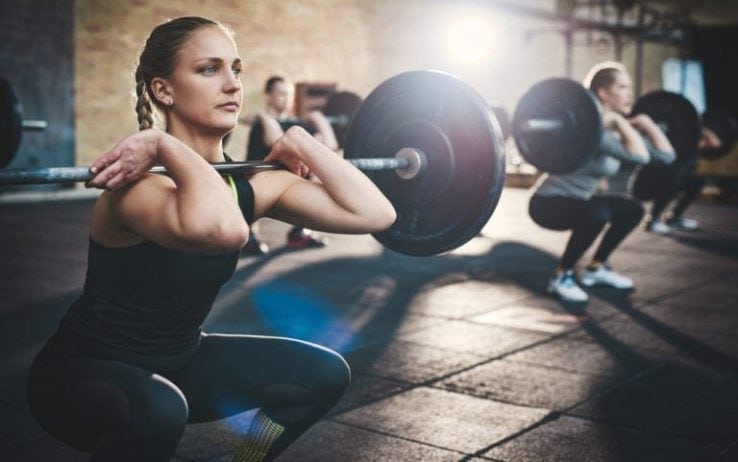 A woman doing squats with a long barbell in the gym