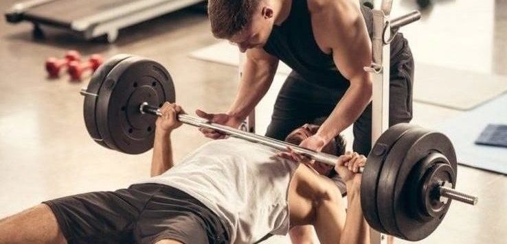 A man bench pressing while his friend helps spot him