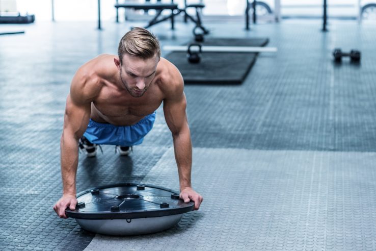 A man in the gym doing core exercises with a balance board