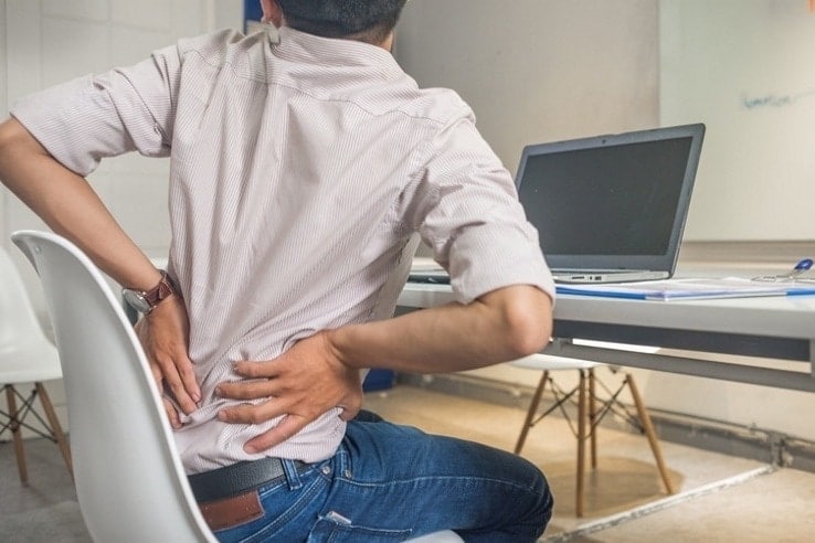 A man sat at his home office having trouble with his lower back