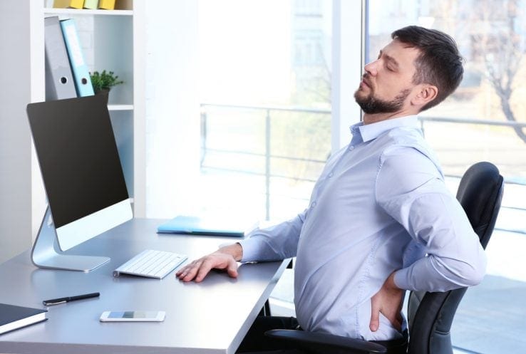 A man sat at his office desk stretching out his bad back