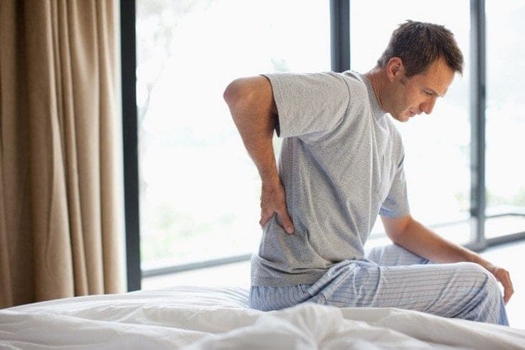 A man sat on his bed having issues with back pain