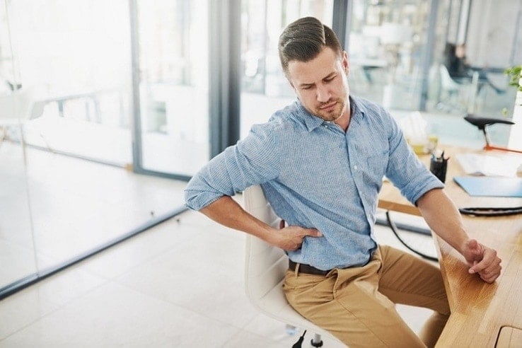 A man suffering from hip pain while sat at his desk