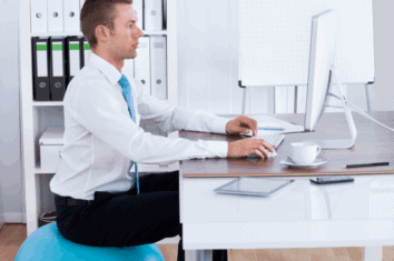 A man using a yoga ball to improve his posture while sat at his office desk