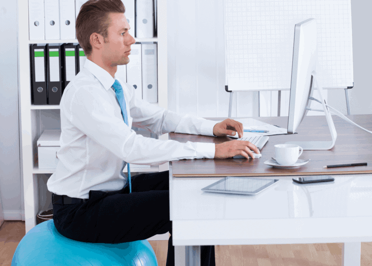 A man using a yoga ball to improve his posture while sat at his office desk