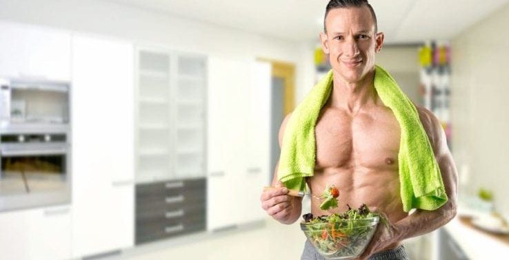 A shirtless man eating salad before he goes to exercise