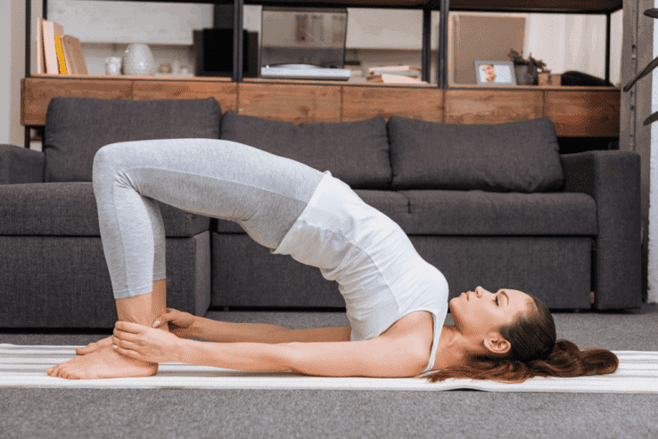 A woman doing a bridge yoga pose in her living room