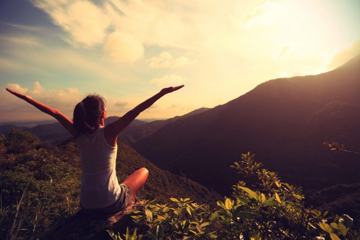 A woman in a sitting yoga pose position on top of a mountain