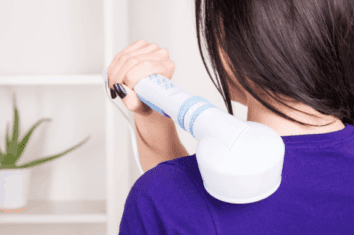 A woman massaging her own shoulder with a handheld massager