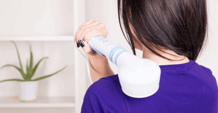 A woman massaging her own shoulder with a handheld massager