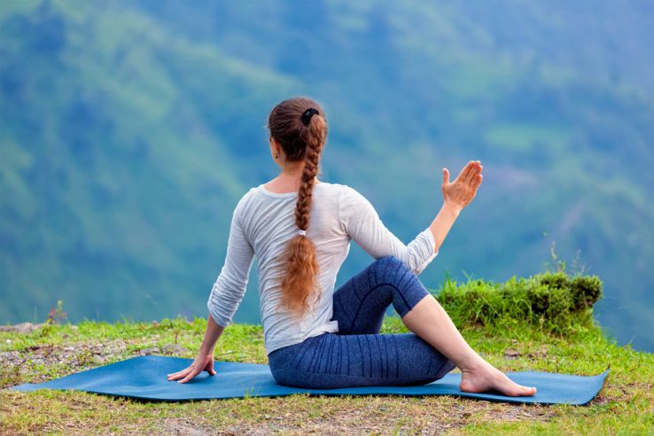 A woman on a yoga mat doing a seated spinal twist pose