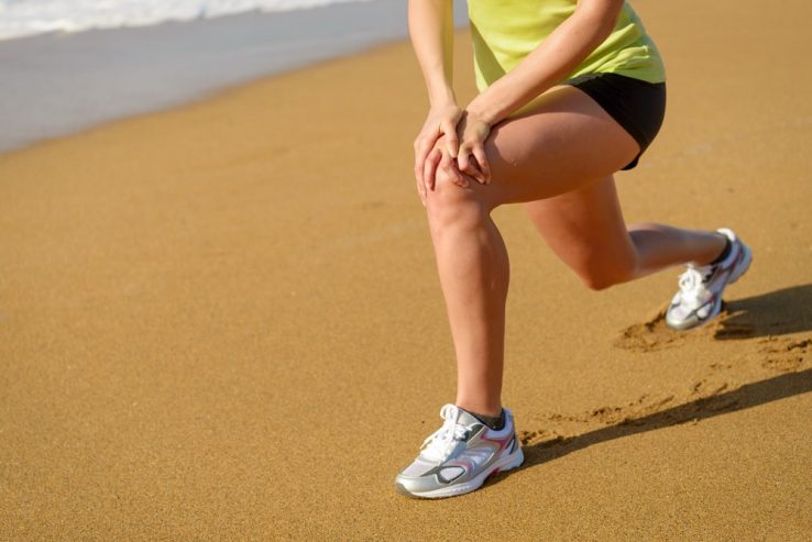 A runner on the beach stretching out her knee