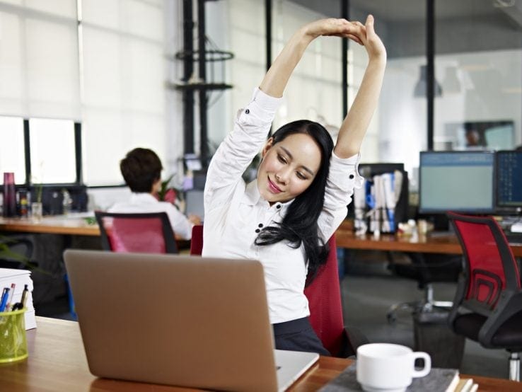 A woman sat at her desk stretching up to the air