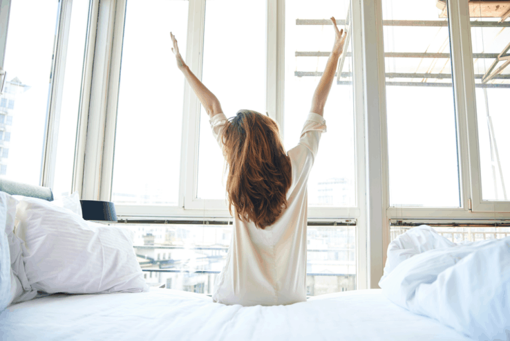 A woman stretching her back as she gets out of bed