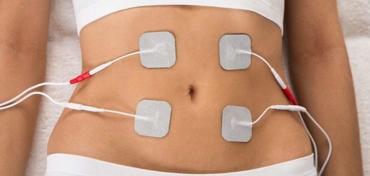 A woman using an electrical muscle stimulation machine on her stomach