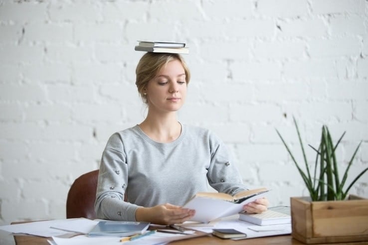A young woman balancing books on top of her head