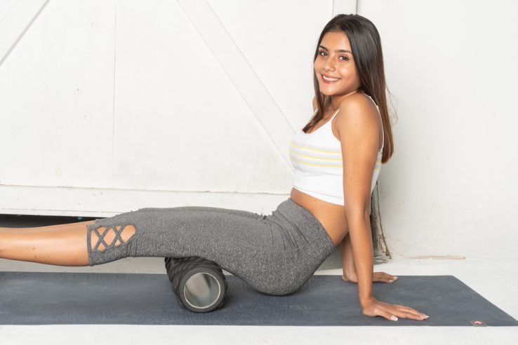 A young woman using a foam roller to stretch out her hamstrings