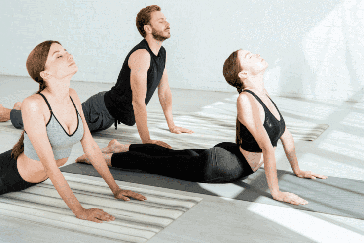 Three people doing the same yoga pose together to stretch their backs