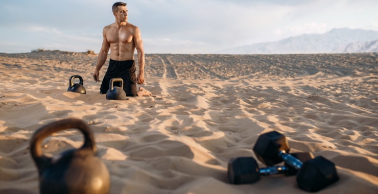 a man exercising on the beach with dumbbells and kettlebells
