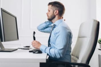 a man sitting in a chair rubbing his neck because of his bad posture