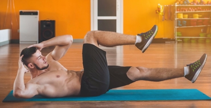 man doing sit-ups on the floor on a blue mat
